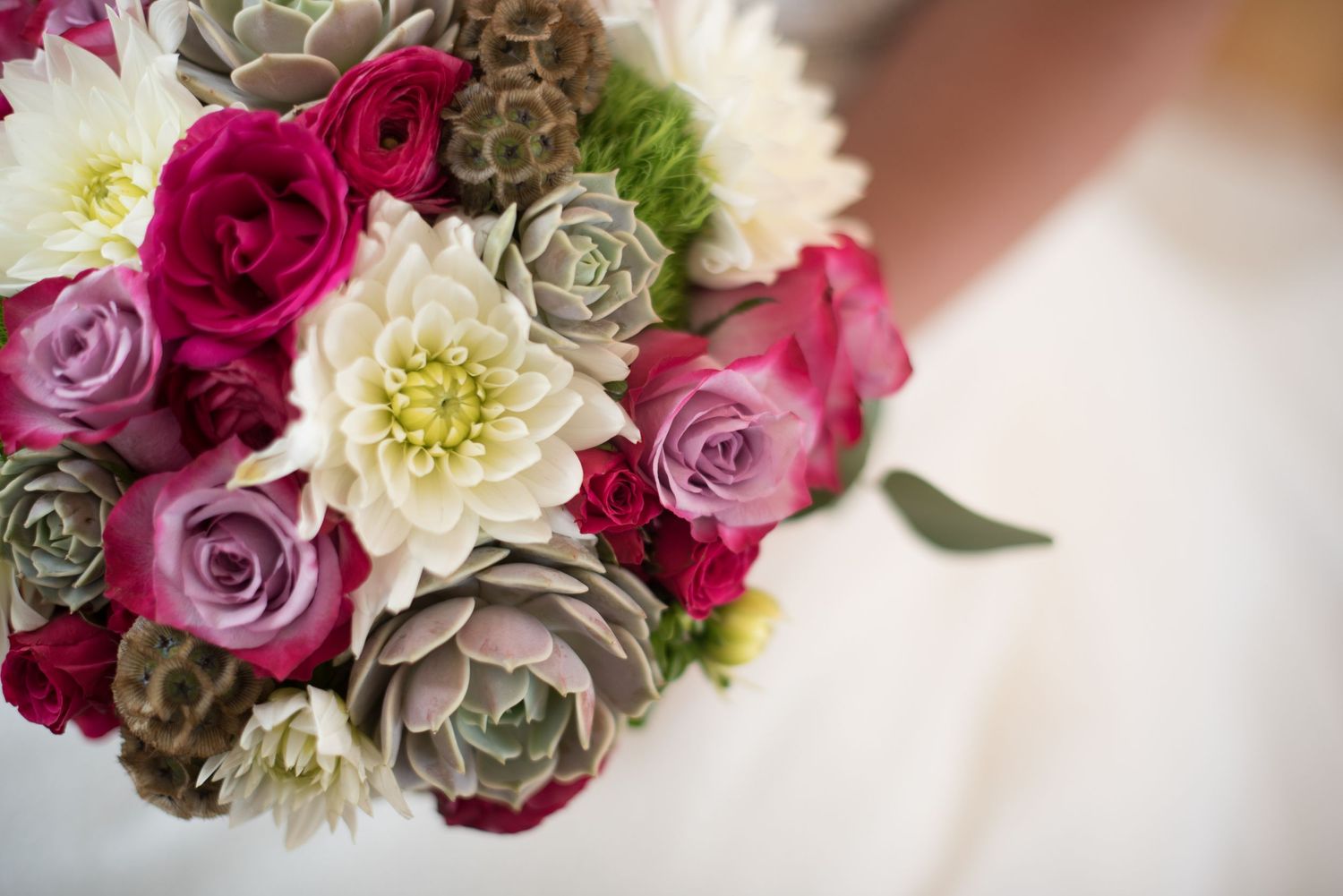 Bridal bouquet featuring succulents, pink roses, dahlias, and white flowers close-up.
