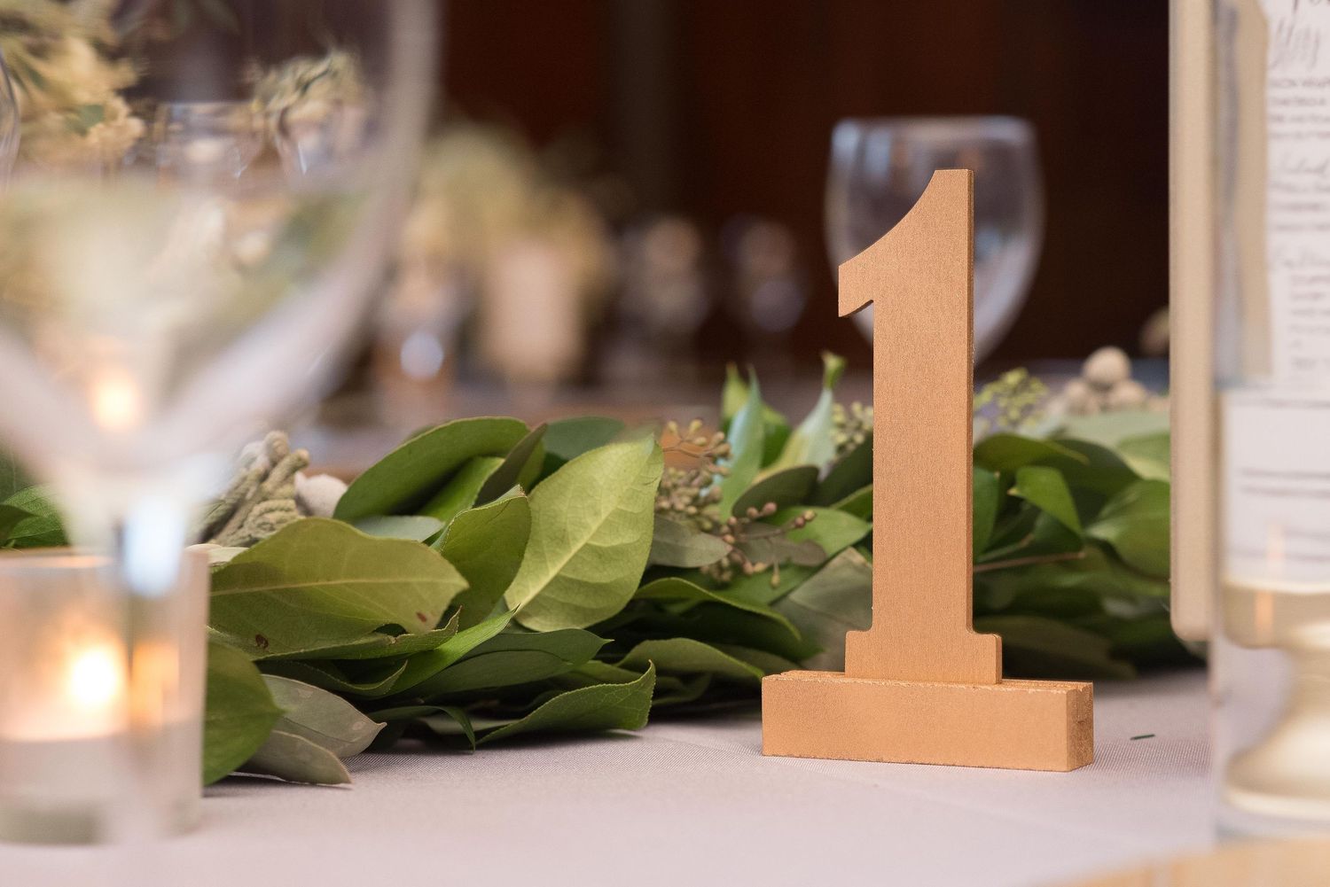 Gold number one table marker with green leaf garland centerpiece at an elegant wedding reception.