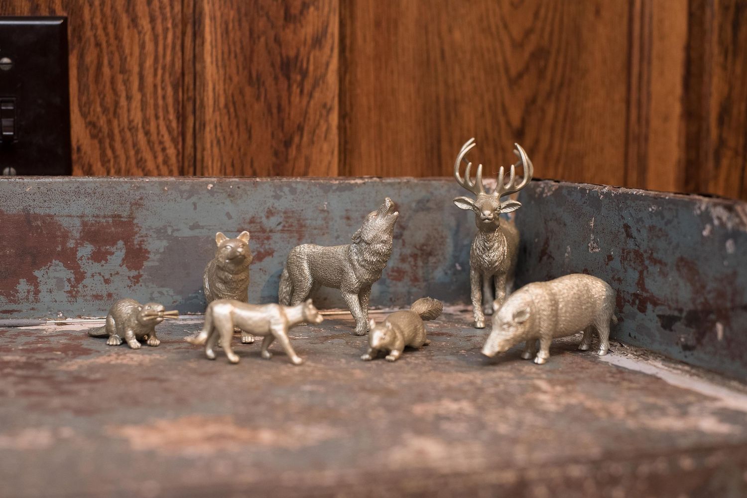 Small gold painted plastic wild animal figurines including a deer, boar, lion, and bear arranged on a rustic weathered surface.