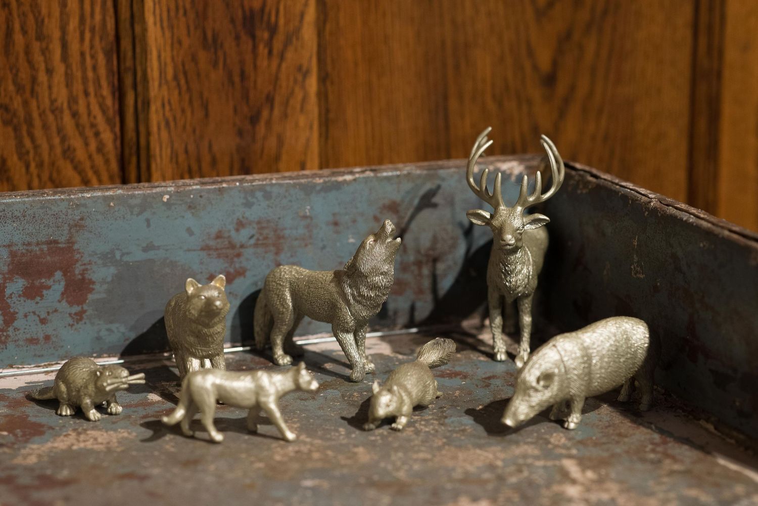 Collection of small silver metallic animal figurines including a deer, pigs, and fox displayed on a rustic blue surface.