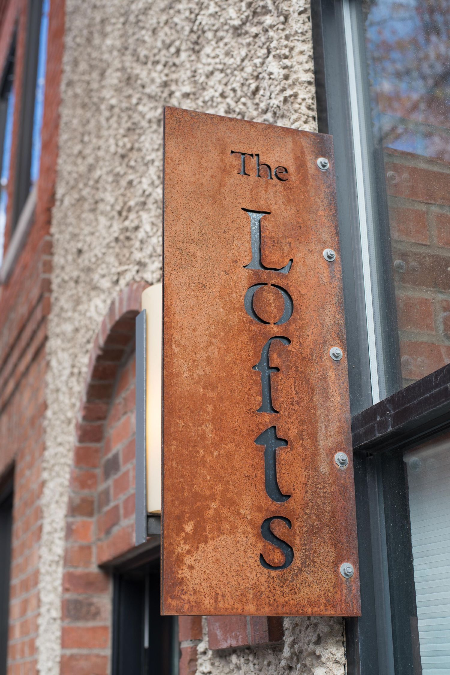 Rustic metal sign reading The Lofts mounted on a brick building exterior with weathered patina finish.