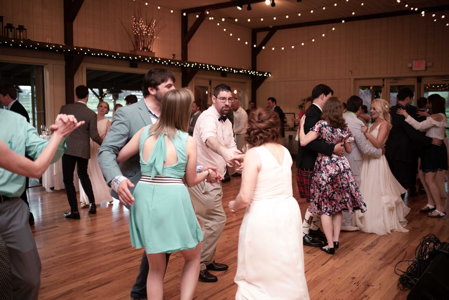 Guests dancing at a rustic barn wedding reception with string lights and a bride in a white gown.