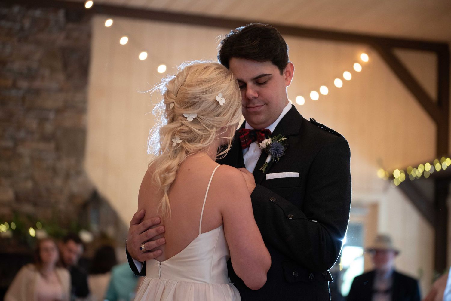 Bride and groom share their first dance at a romantic wedding reception with warm string lights in a rustic barn venue.