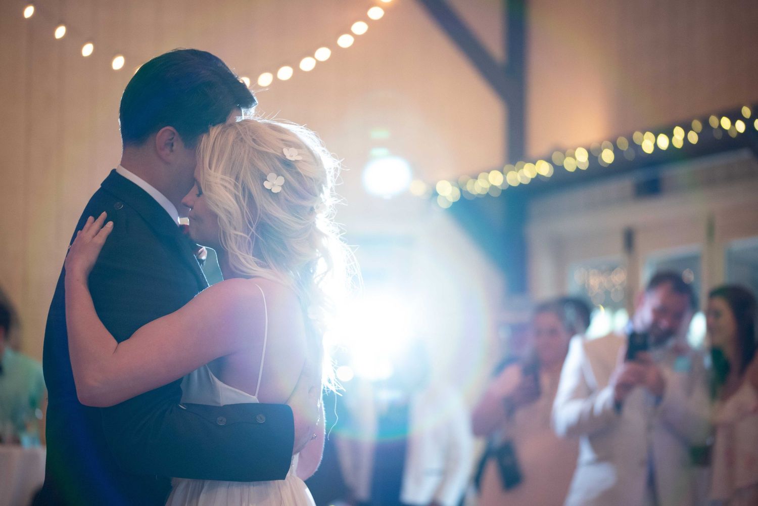 Couple sharing their first dance at a romantic wedding reception with warm string lights glowing in the background.