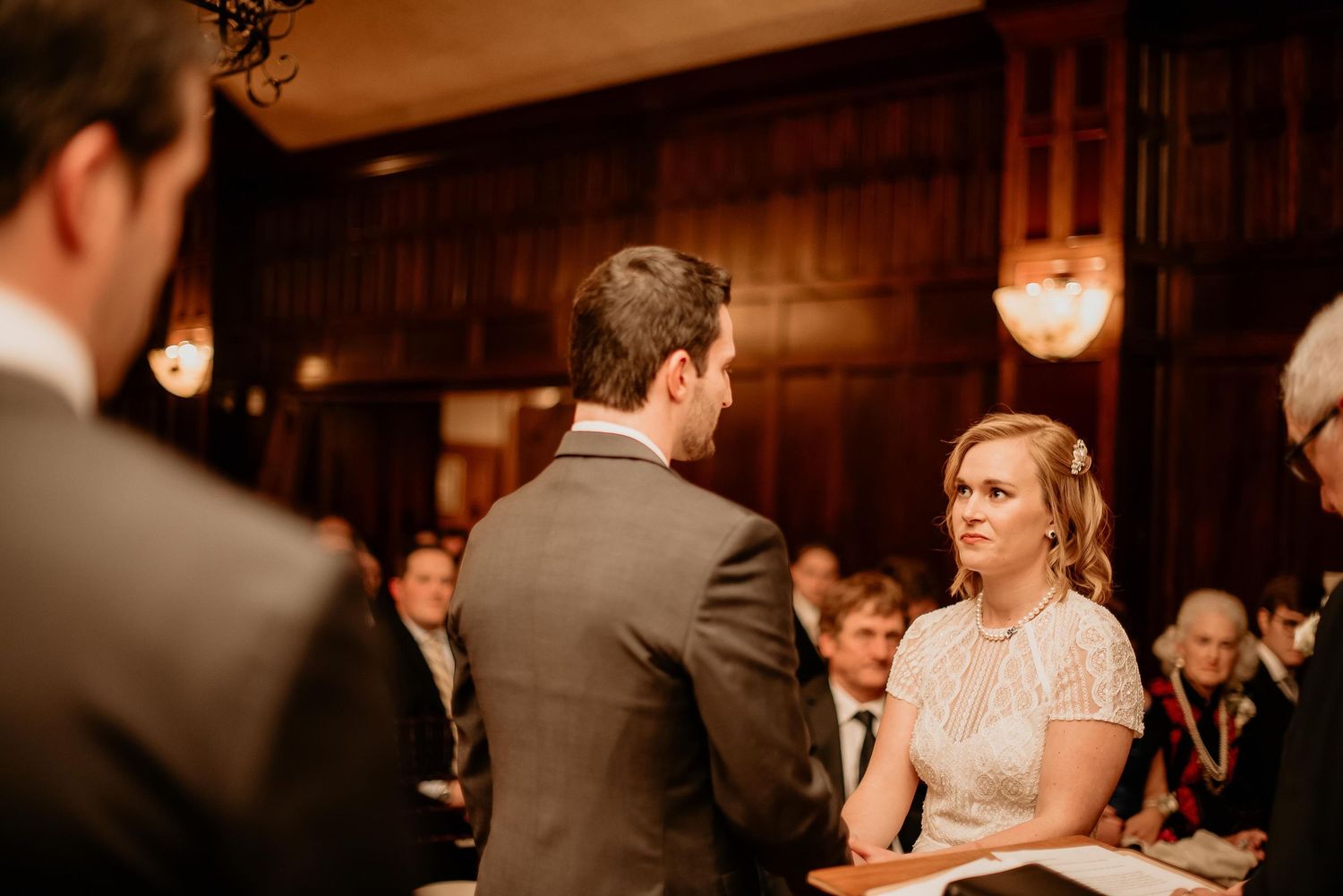 Bride and groom exchanging vows during an intimate wedding ceremony in an elegant wood-paneled venue.
