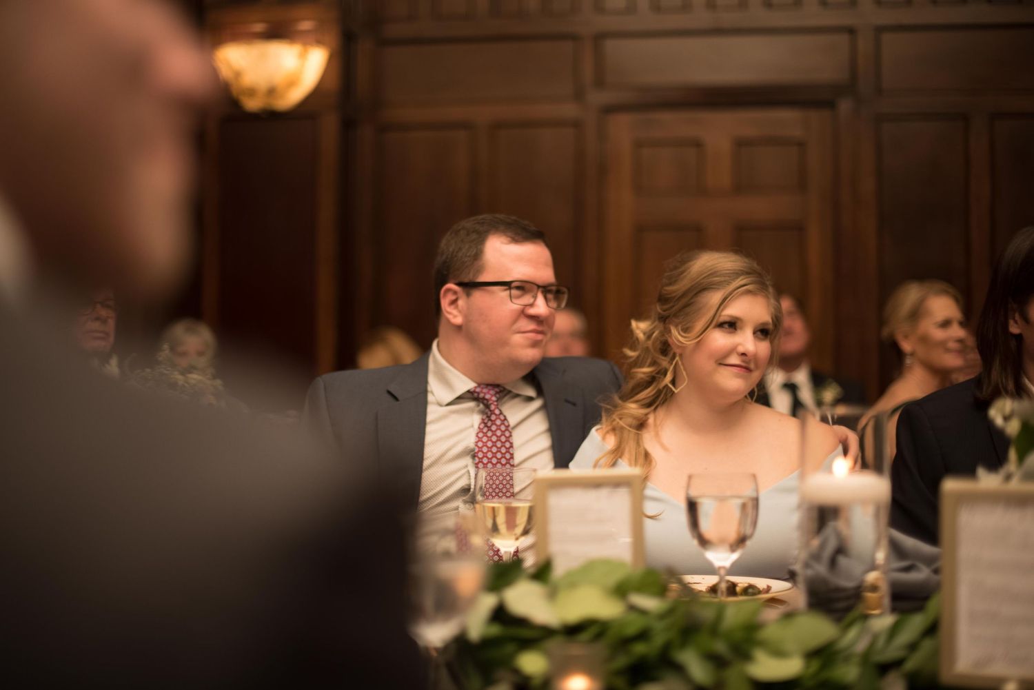 Couple smiling at a wedding reception dinner table with candles and floral centerpieces.