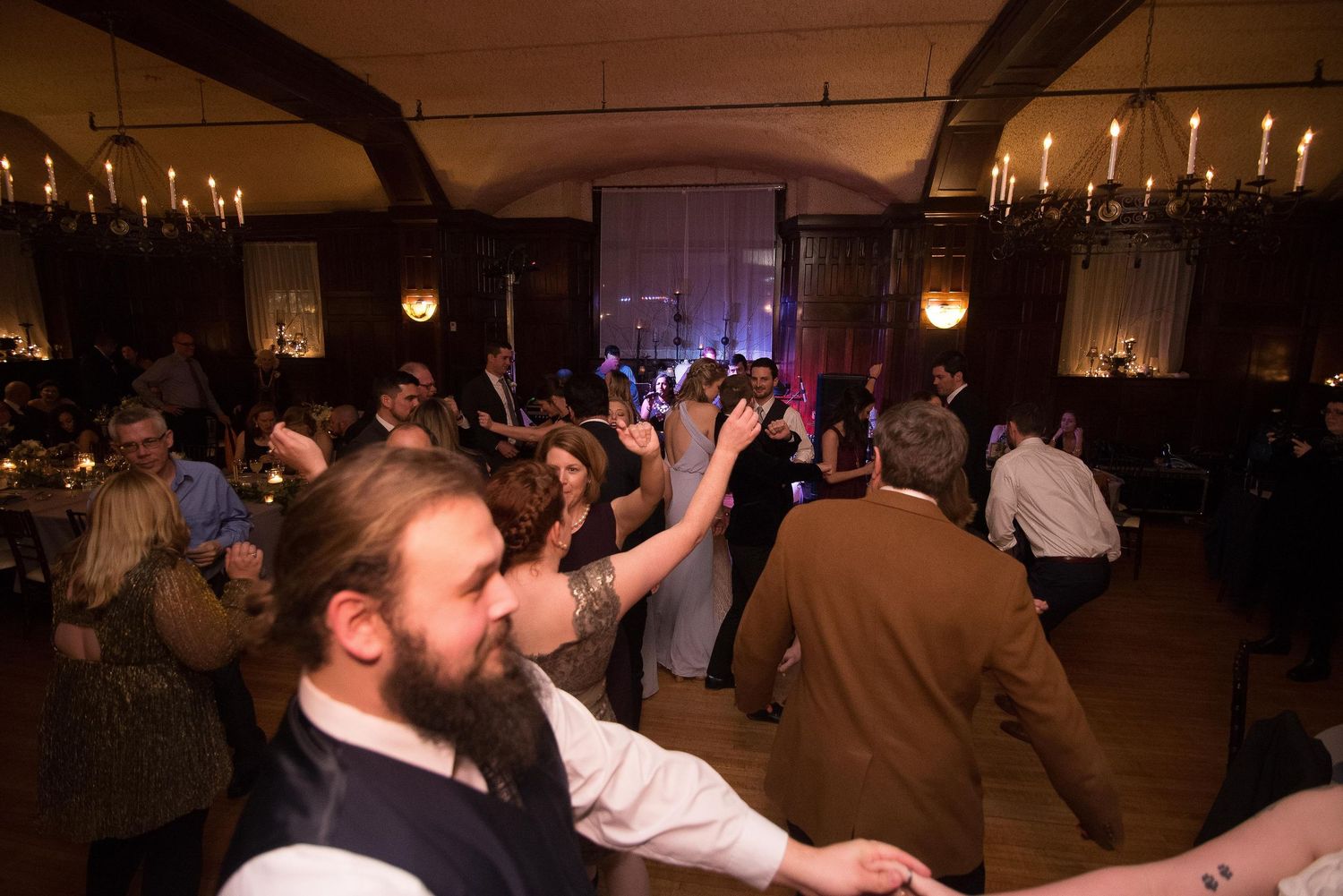 Guests dancing at a candlelit wedding reception in a rustic venue with warm ambient lighting.
