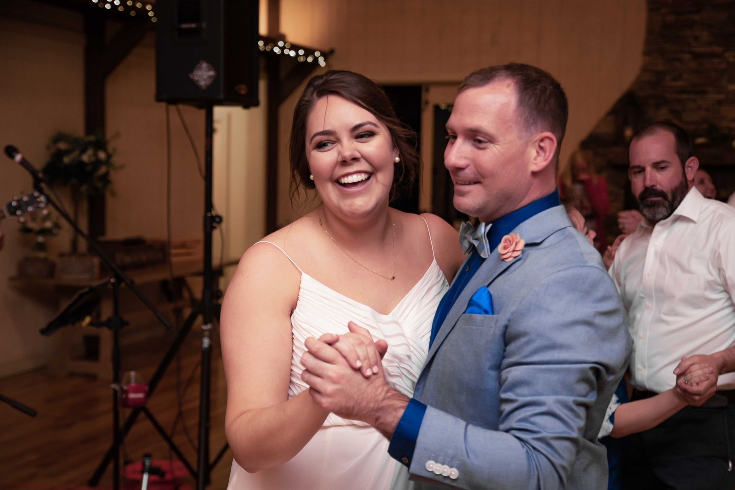 A bride and groom share a joyful first dance at their wedding reception in a warmly lit venue.