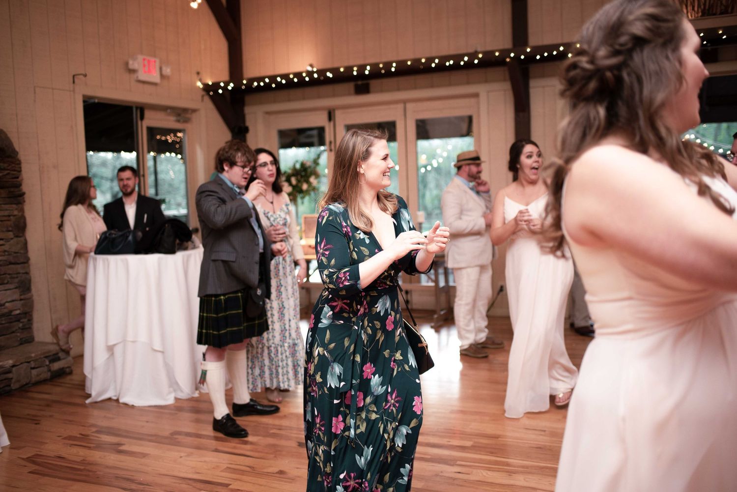 Guests mingle at an elegant wedding reception in a rustic barn venue with string lights and hardwood floors.