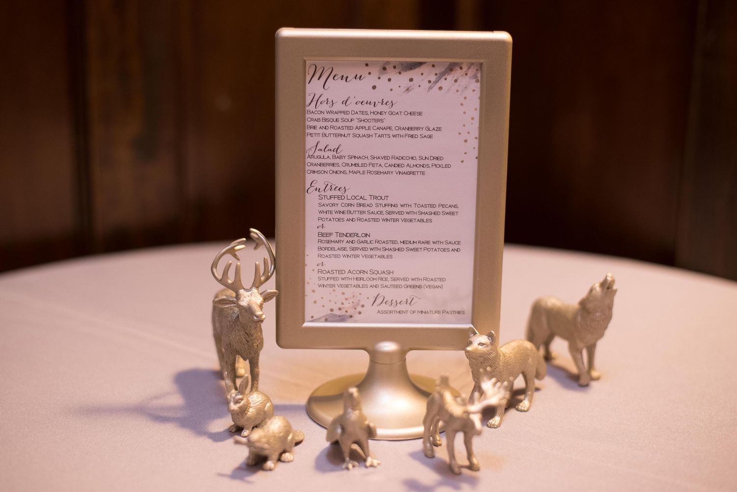 Gold animal figurines surround a framed wedding menu card on a white tablecloth at an elegant reception.