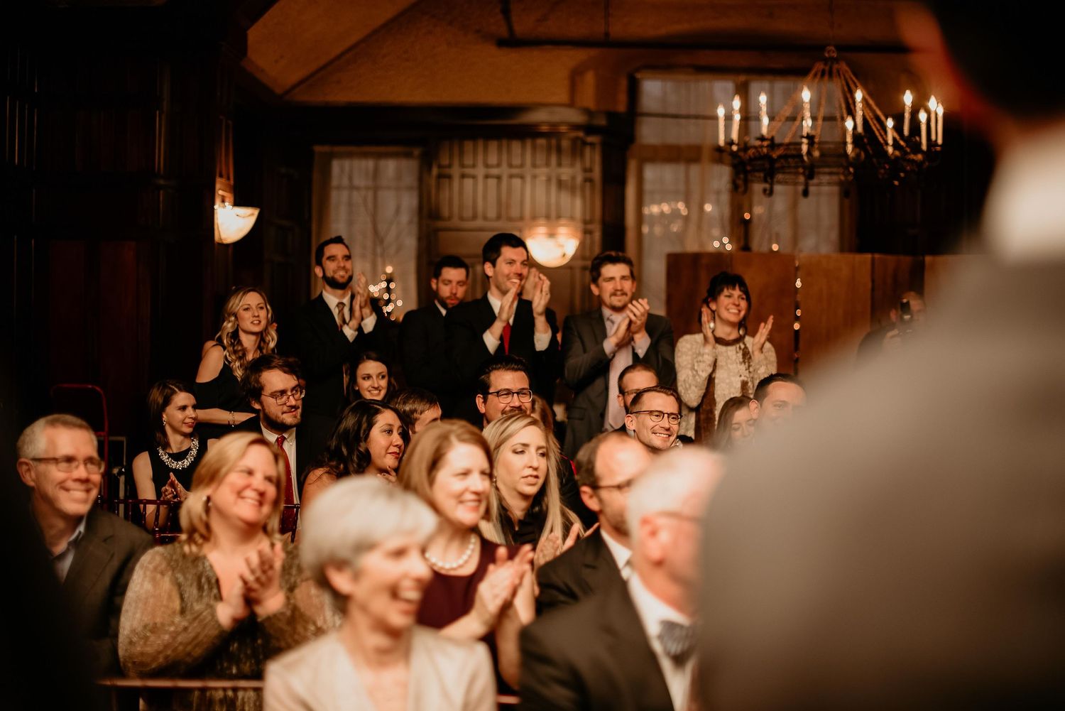 Wedding guests clapping and smiling in a warmly lit venue during a ceremony celebration.