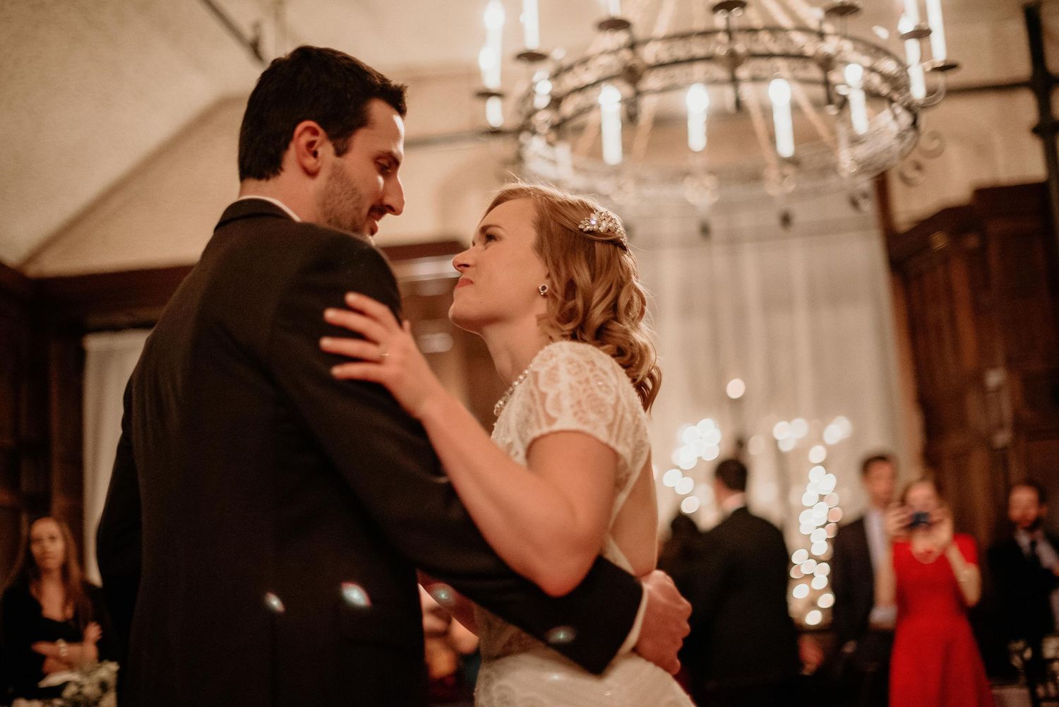 Bride and groom share first dance under elegant chandelier at romantic indoor wedding reception.