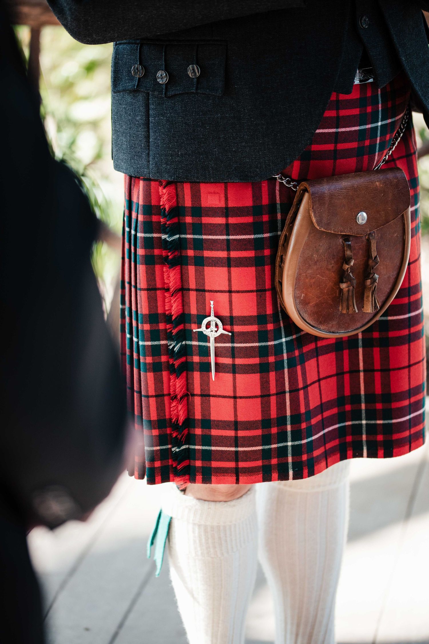 Man wearing traditional Scottish red tartan kilt with leather sporran and white knee-high socks.