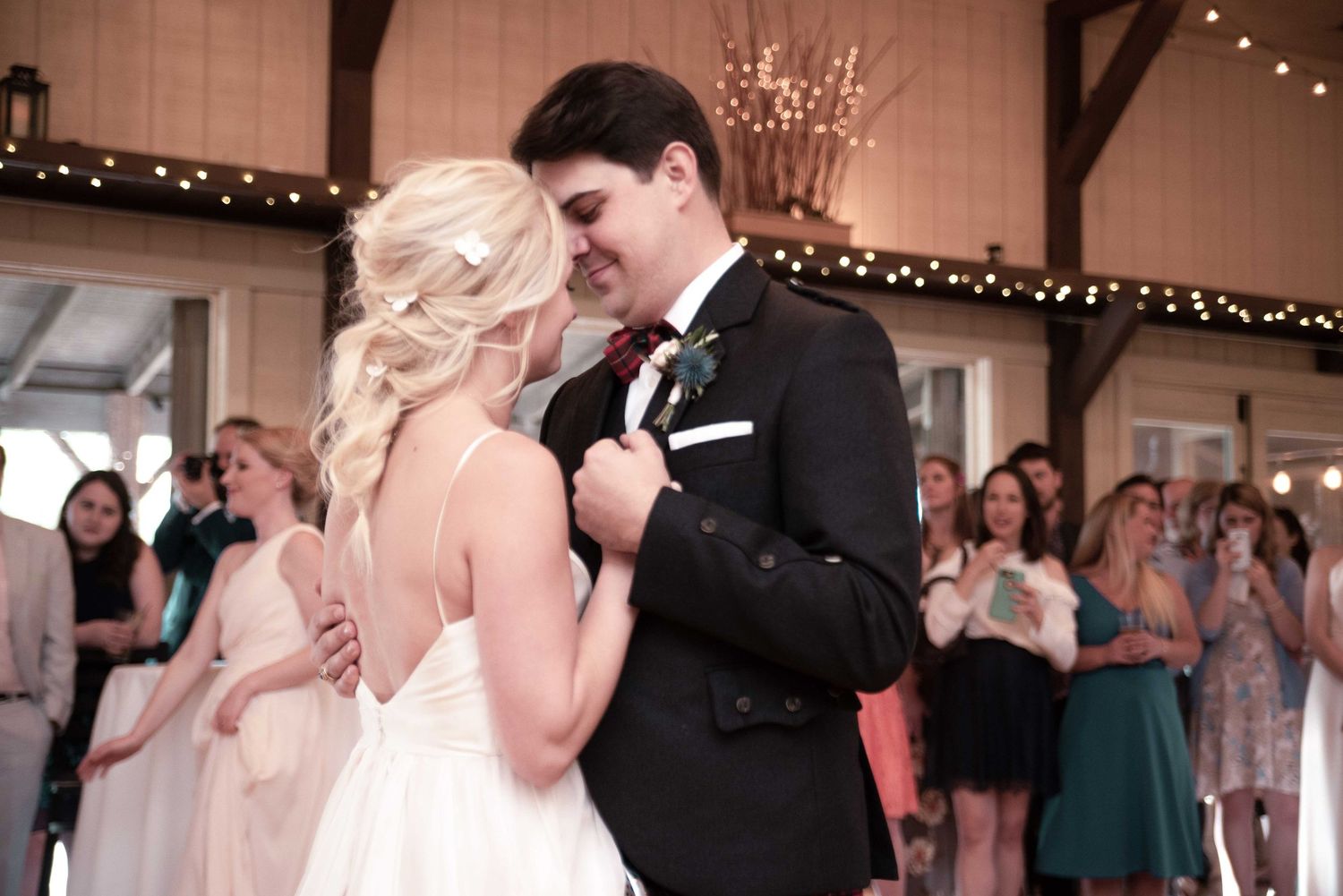 A bride and groom share their first dance surrounded by guests at an elegant wedding reception.