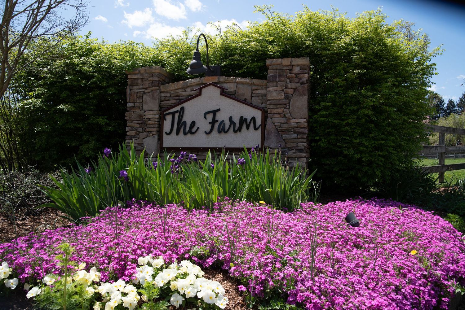 Colorful flower garden surrounds stone entrance sign for The Farm wedding venue.