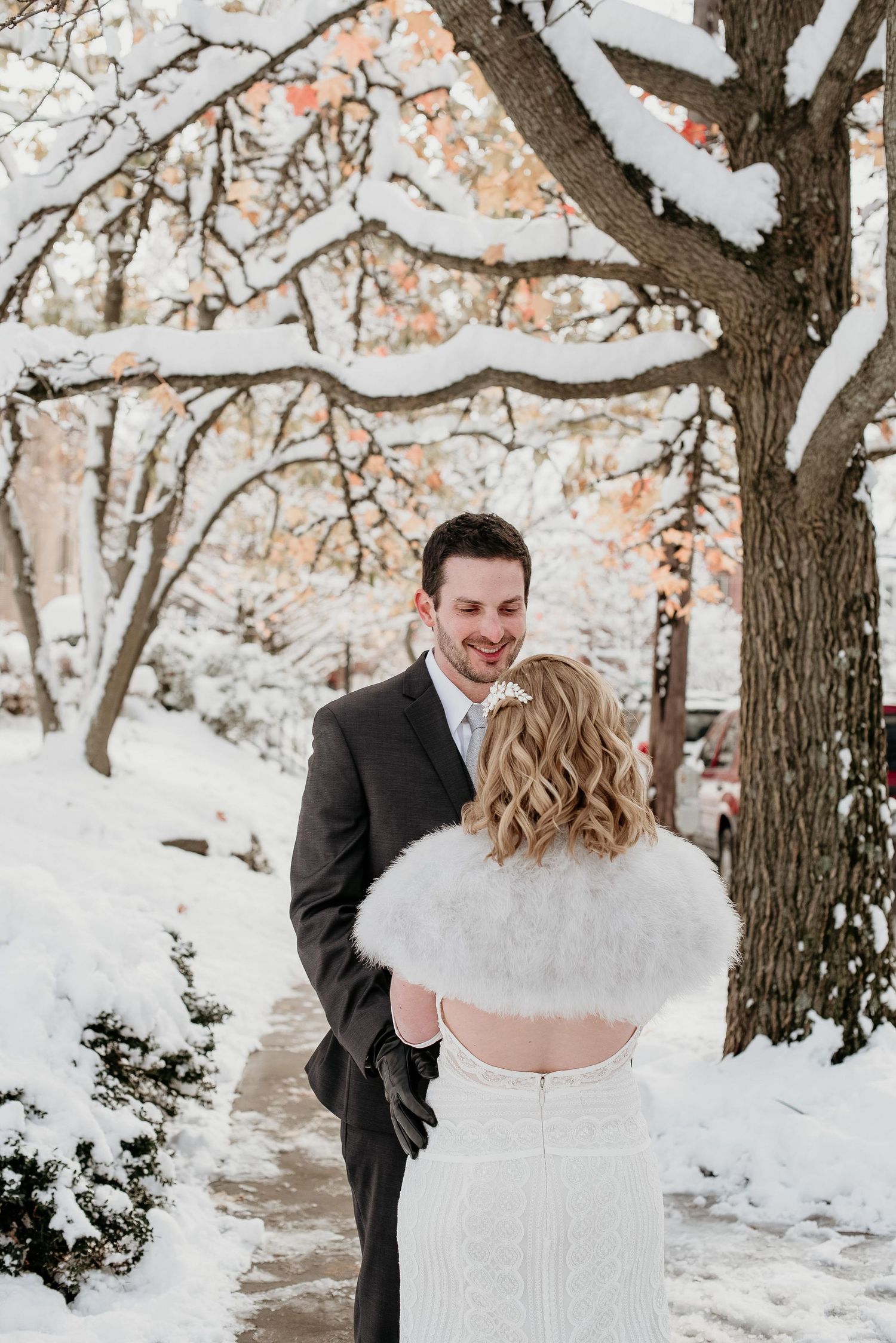 Couple shares a romantic first look moment in a snowy winter wonderland, bride in white gown with fur wrap.