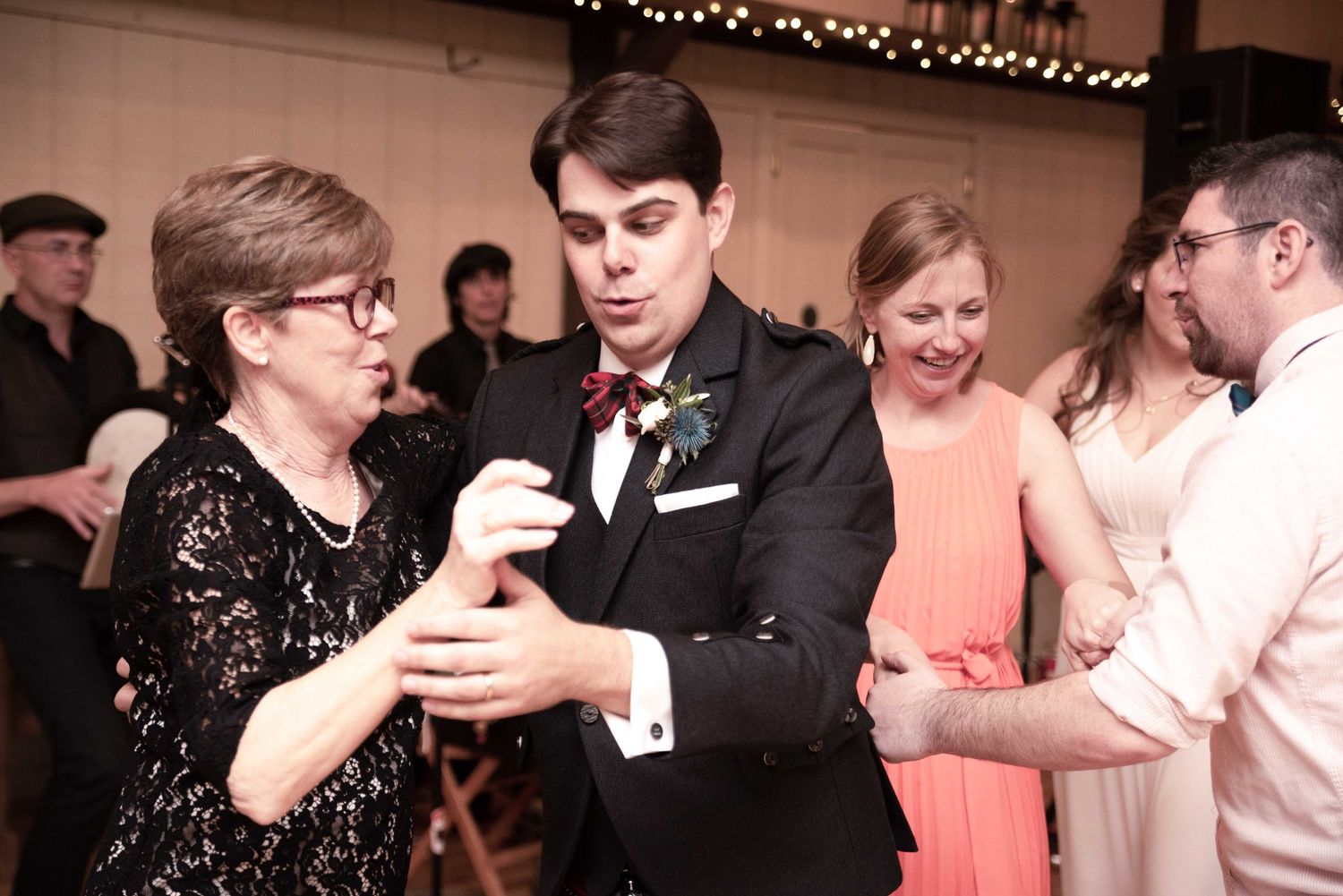 Groom in tuxedo dancing with guests at wedding reception on decorated dance floor.