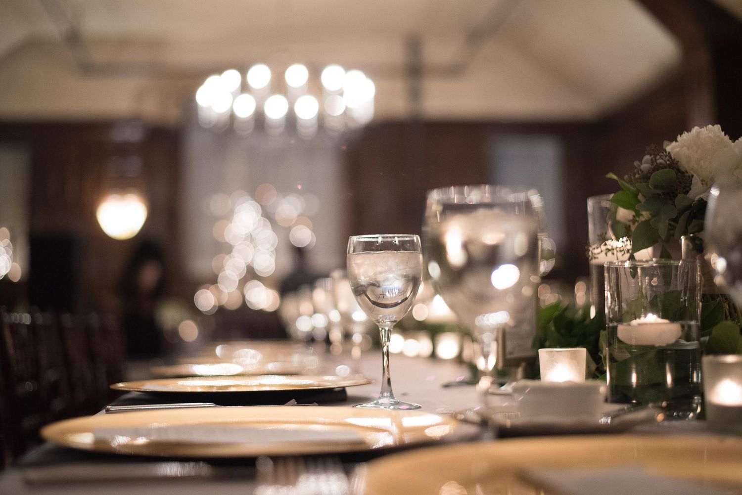 Elegant wedding reception table setting with crystal glassware, white floral centerpieces, and soft candlelight.