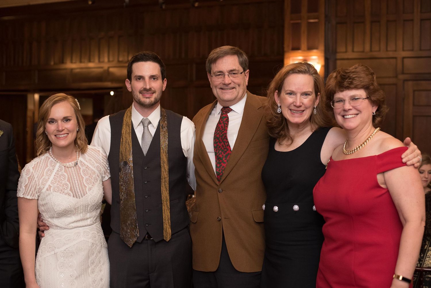 Group of five adults posing together at a formal indoor event, smiling for a photo in an elegant wood-paneled venue.