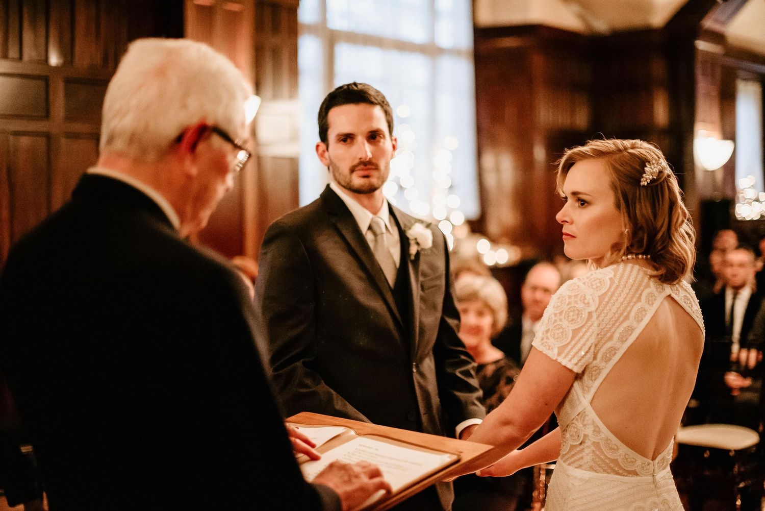 Bride and groom exchange vows before officiant during elegant indoor wedding ceremony.