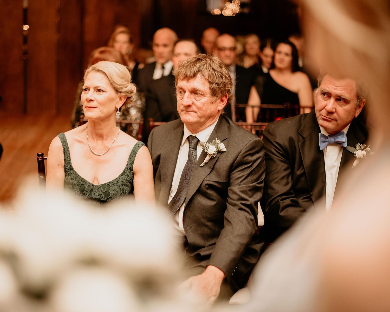 Elegantly dressed wedding guests seated in wooden pews, attentively watching a ceremony unfold.