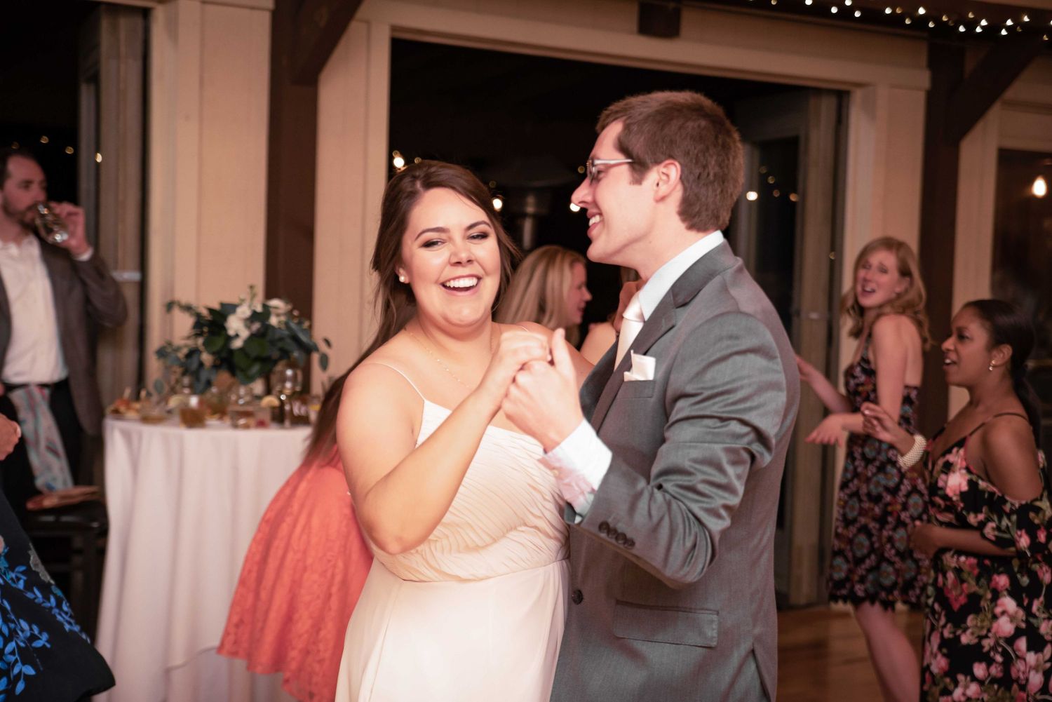 Couple sharing a joyful first dance at wedding reception, bride in white gown laughing with groom in gray suit.
