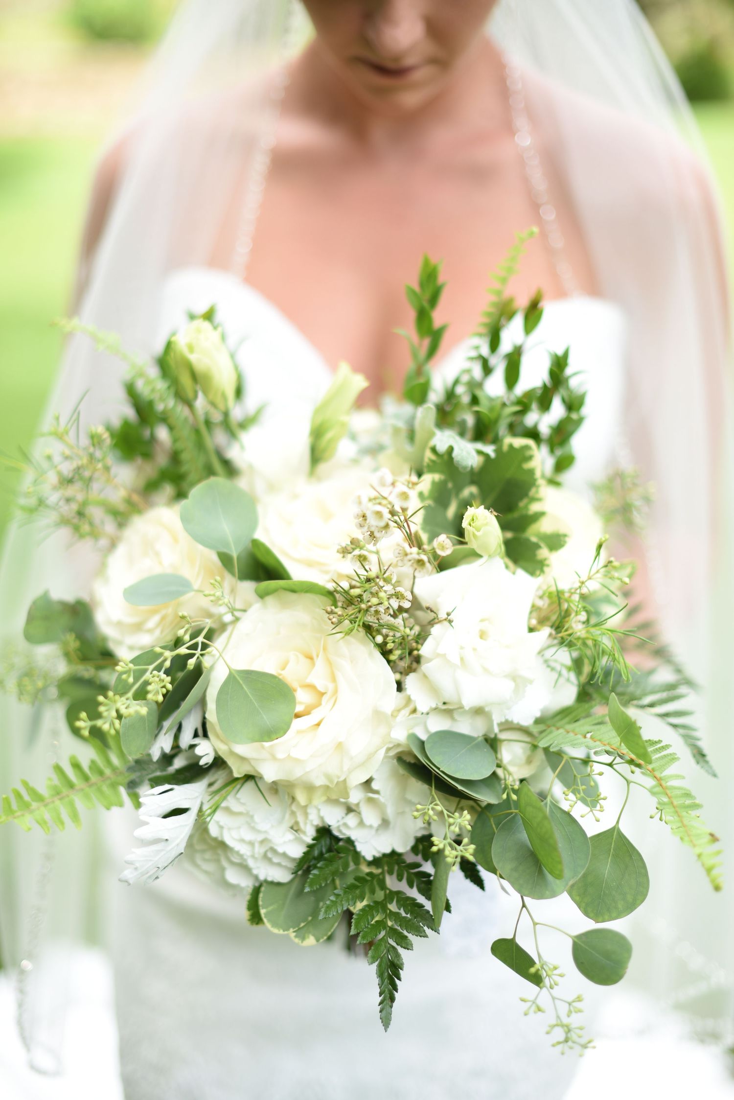 Bride holding a lush white and green wedding bouquet with ferns.