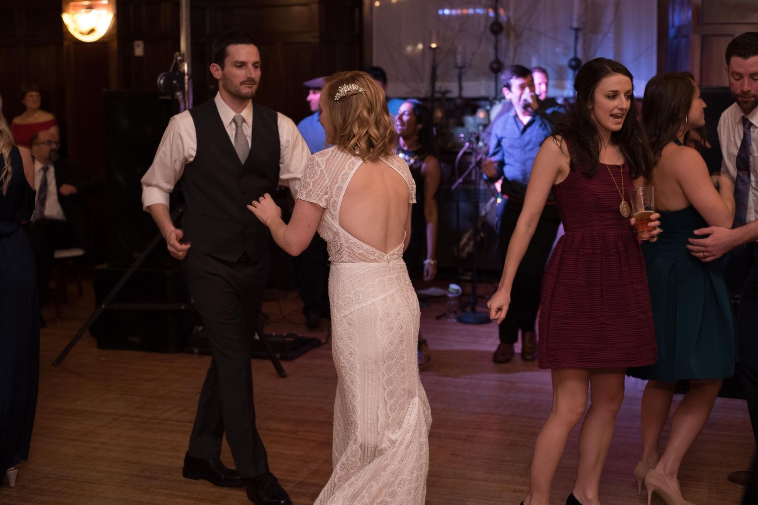 Bride and groom share a romantic first dance at wedding reception with guests dancing nearby.