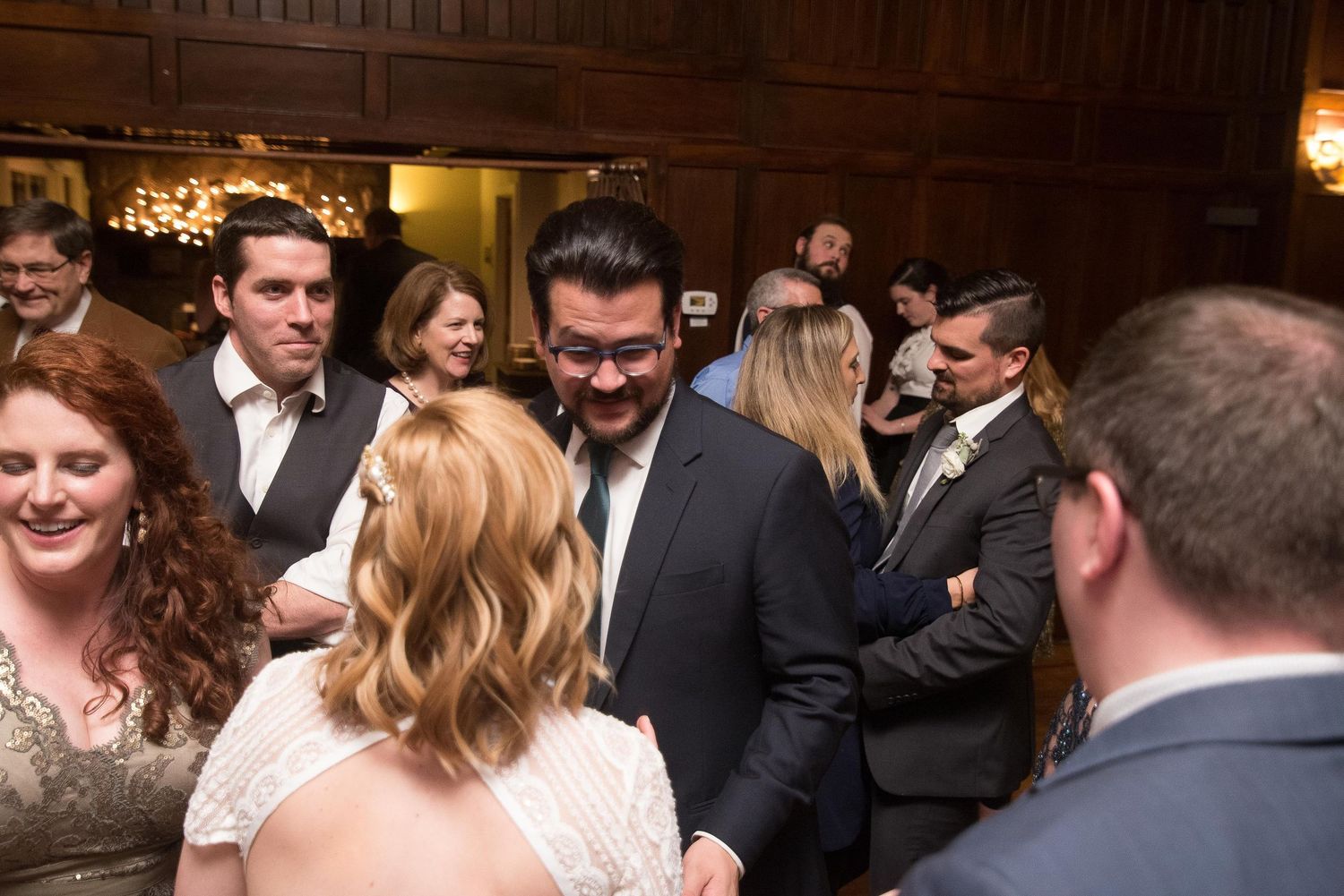 Guests mingling and smiling at an elegant wedding reception in a wood-paneled venue.
