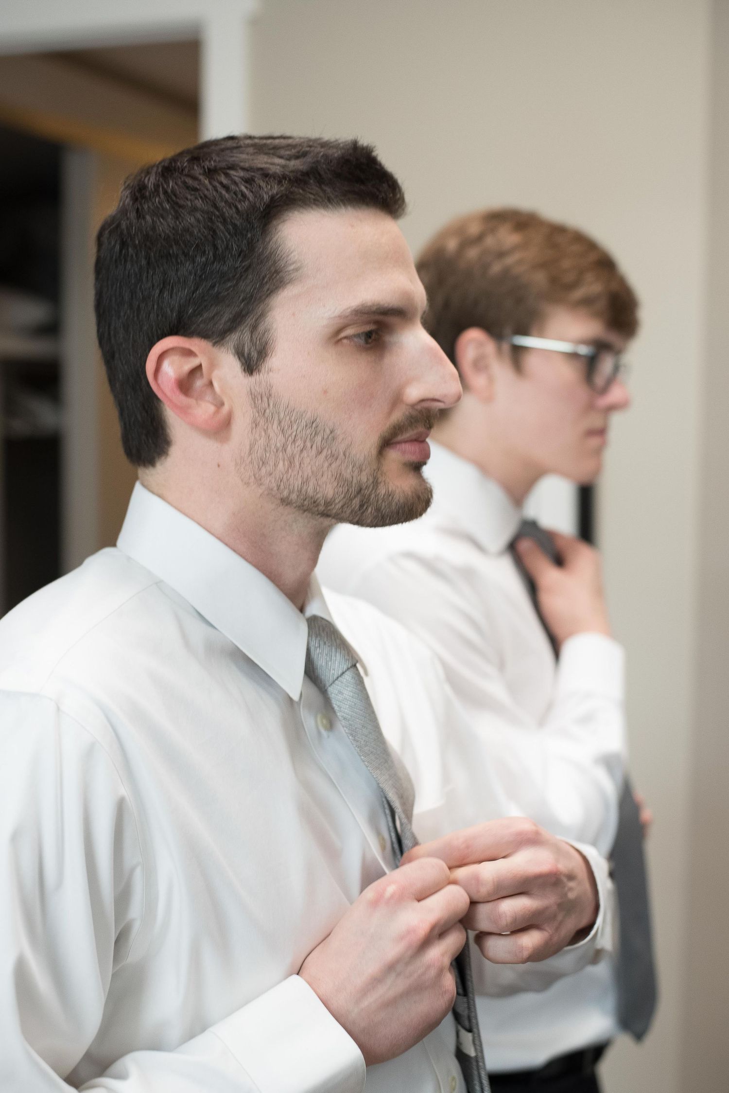 Two men in white dress shirts adjusting their ties, preparing for a formal event.