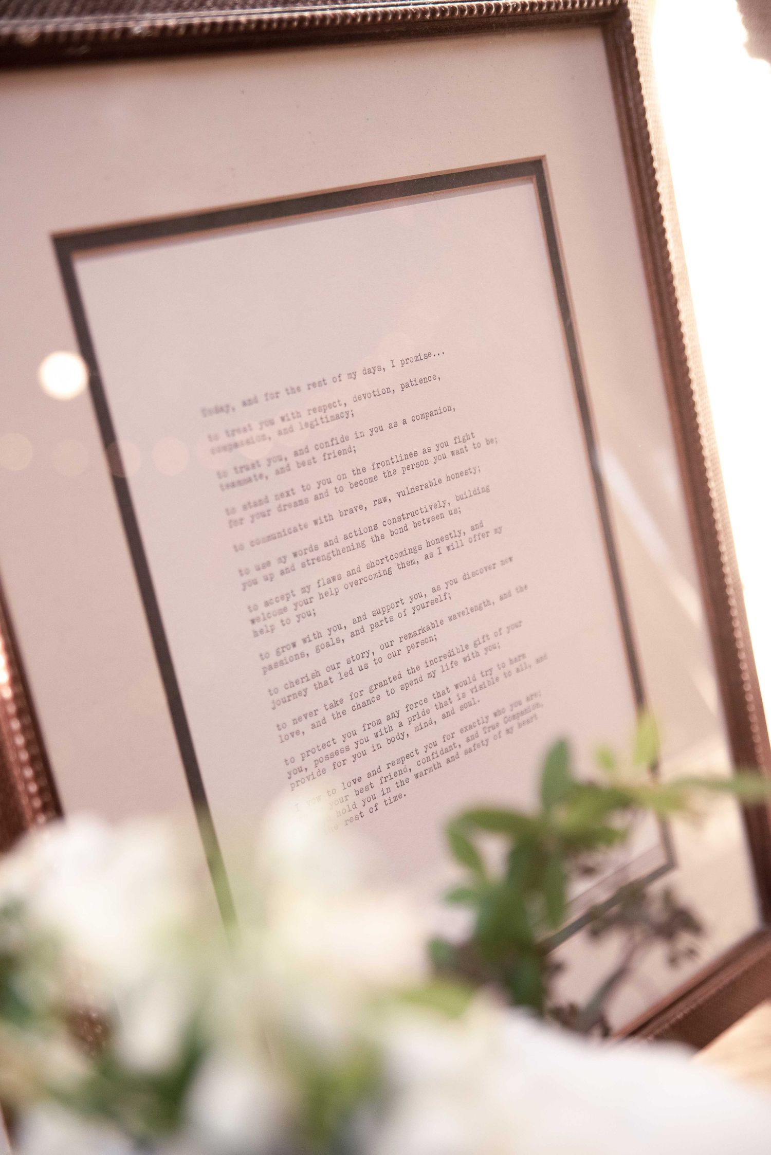 Framed wedding vows displayed in an ornate gold frame surrounded by white floral arrangements at a wedding reception.