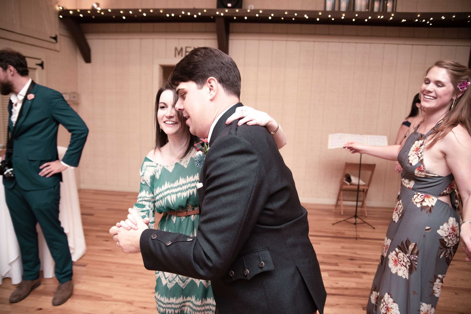 Couple shares a romantic dance at a rustic wedding reception while guests celebrate in the background.