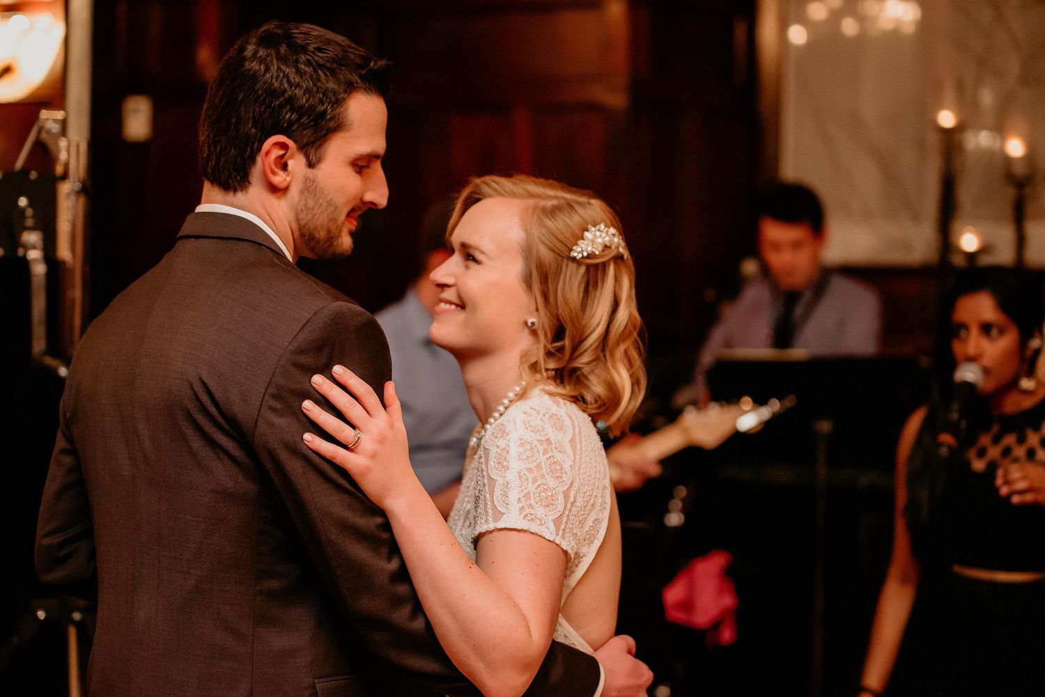 Couple sharing first dance at wedding reception with live band performing in background.