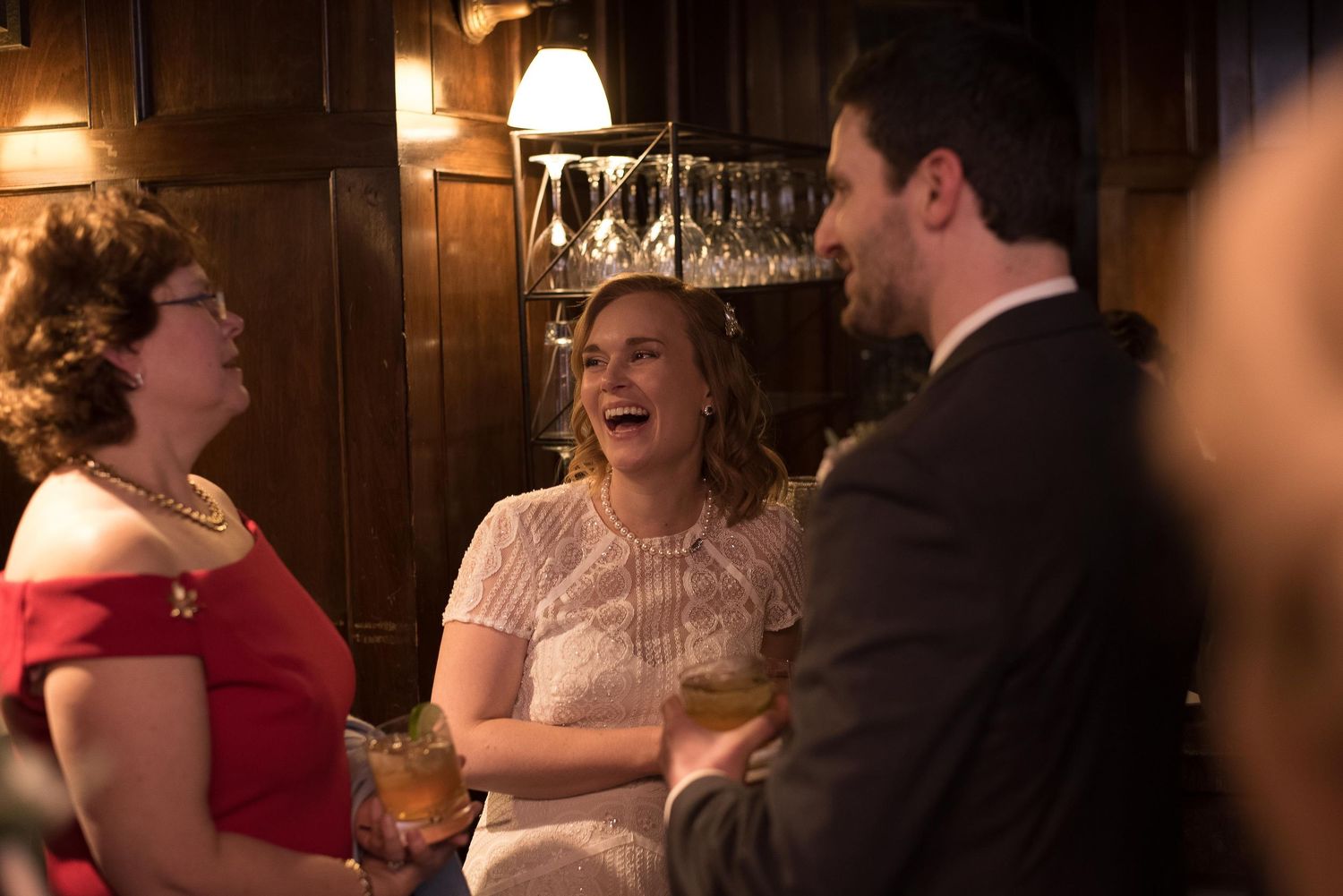 Bride in white dress laughing with guests at elegant wedding reception in wood-paneled venue.