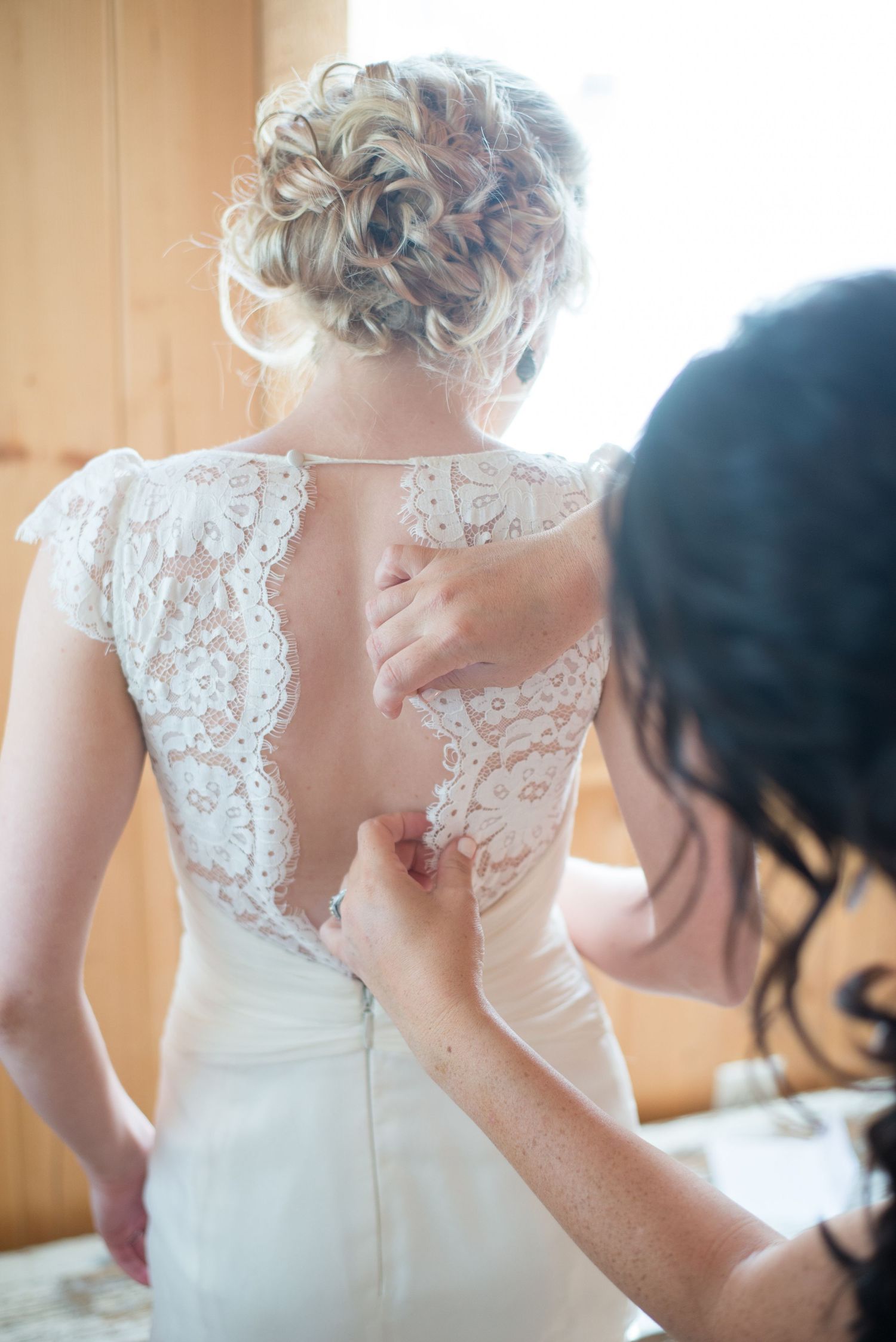 Bridesmaid buttons the intricate lace back of a brides elegant white wedding gown before the ceremony.