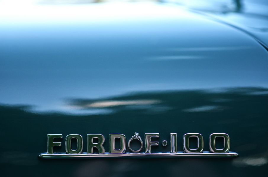 Close-up of a chrome Ford F-100 emblem on a vintage teal truck hood.