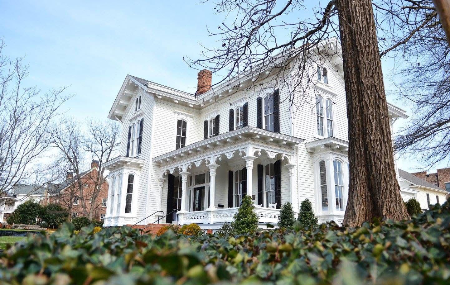 Historic white colonial wedding venue with black shutters surrounded by ivy and mature trees.