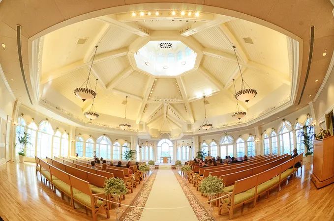Elegant wedding chapel interior with octagonal ceiling, arched windows, wooden pews, and white aisle runner.