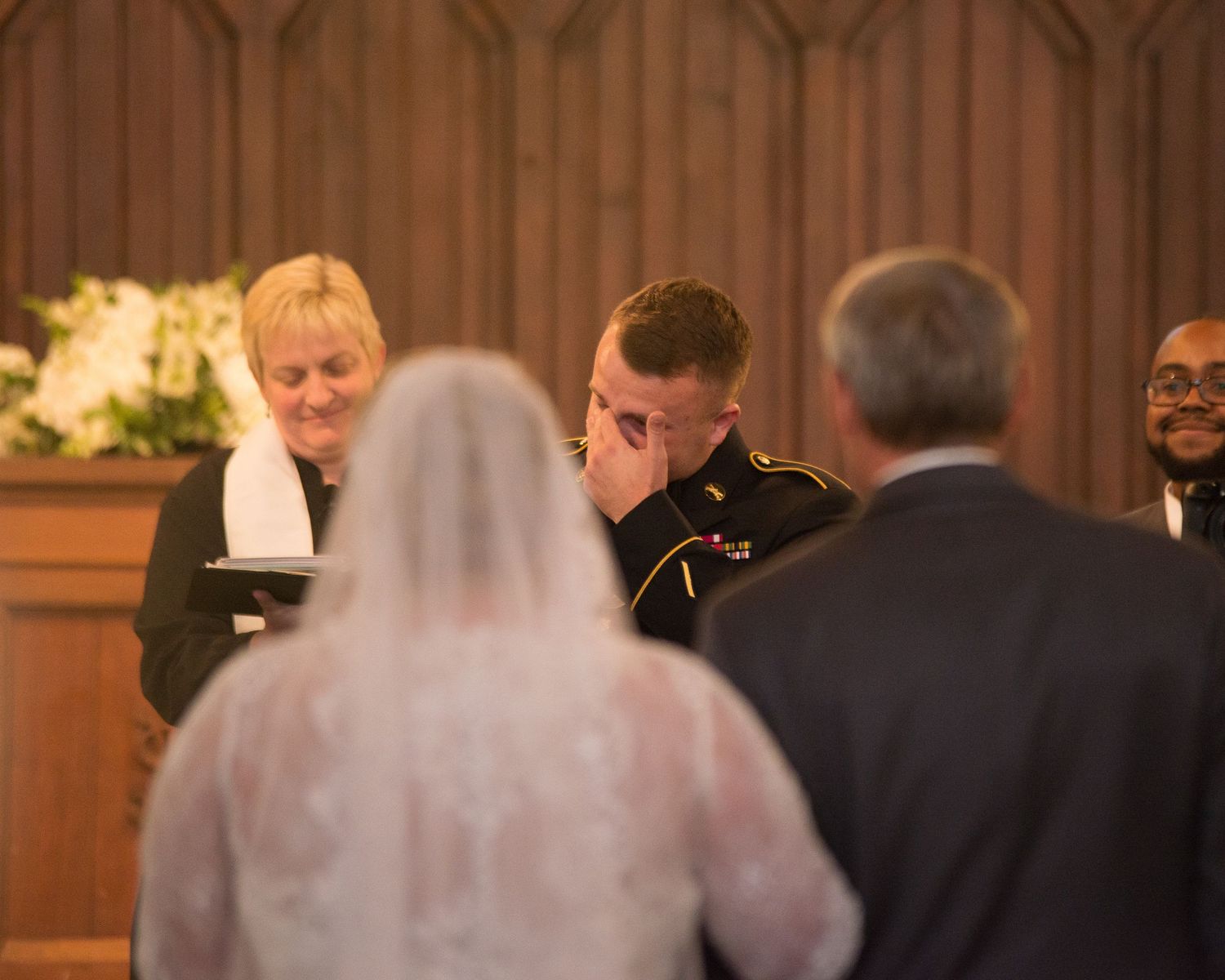 Emotional groom covering his face during wedding ceremony at church altar with officiant present.