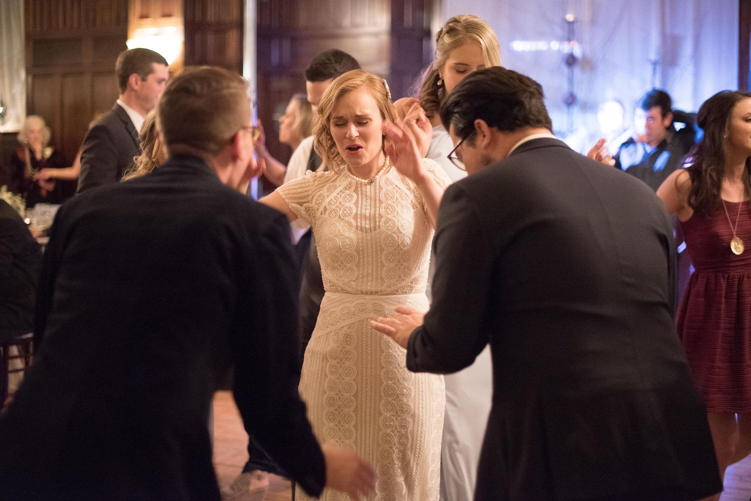 Bride in white lace gown dancing with guests at elegant wedding reception celebration.