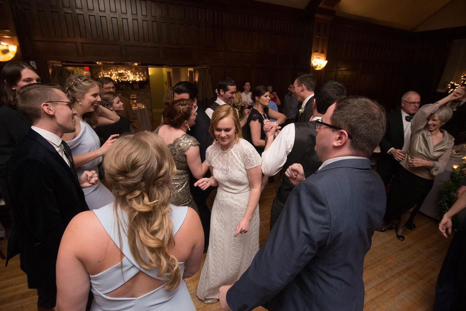Guests dancing joyfully at a wedding reception in an elegant wood-paneled ballroom venue.