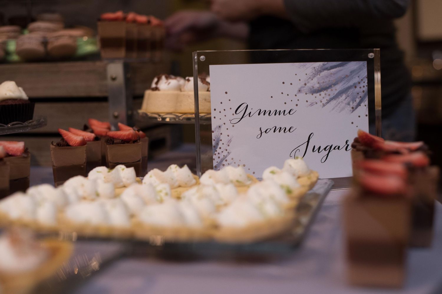 Wedding dessert table with macarons and sweets beside a decorative sign reading Gimme Some Sugar.