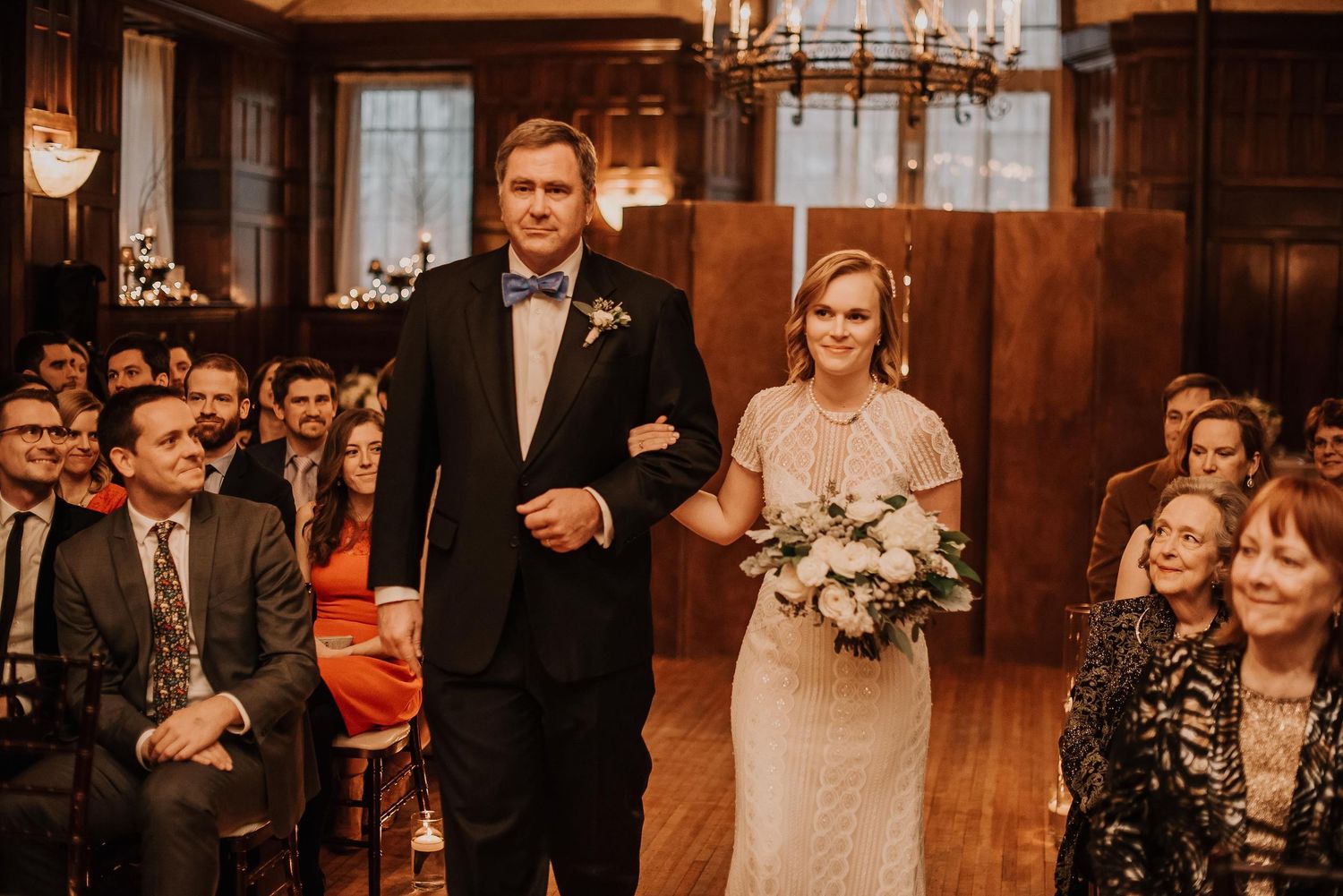 Bride and groom walking down the aisle at an elegant indoor wedding ceremony with guests seated on both sides.