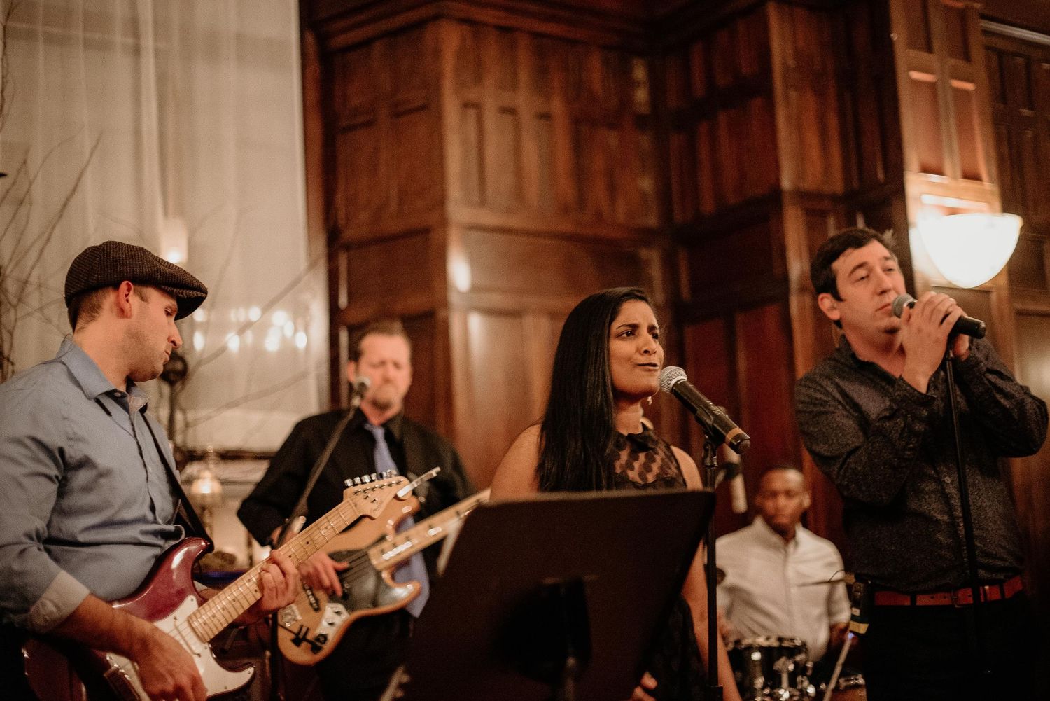 Live band performing at elegant venue with guitarist, female vocalist, and male singer with microphone.