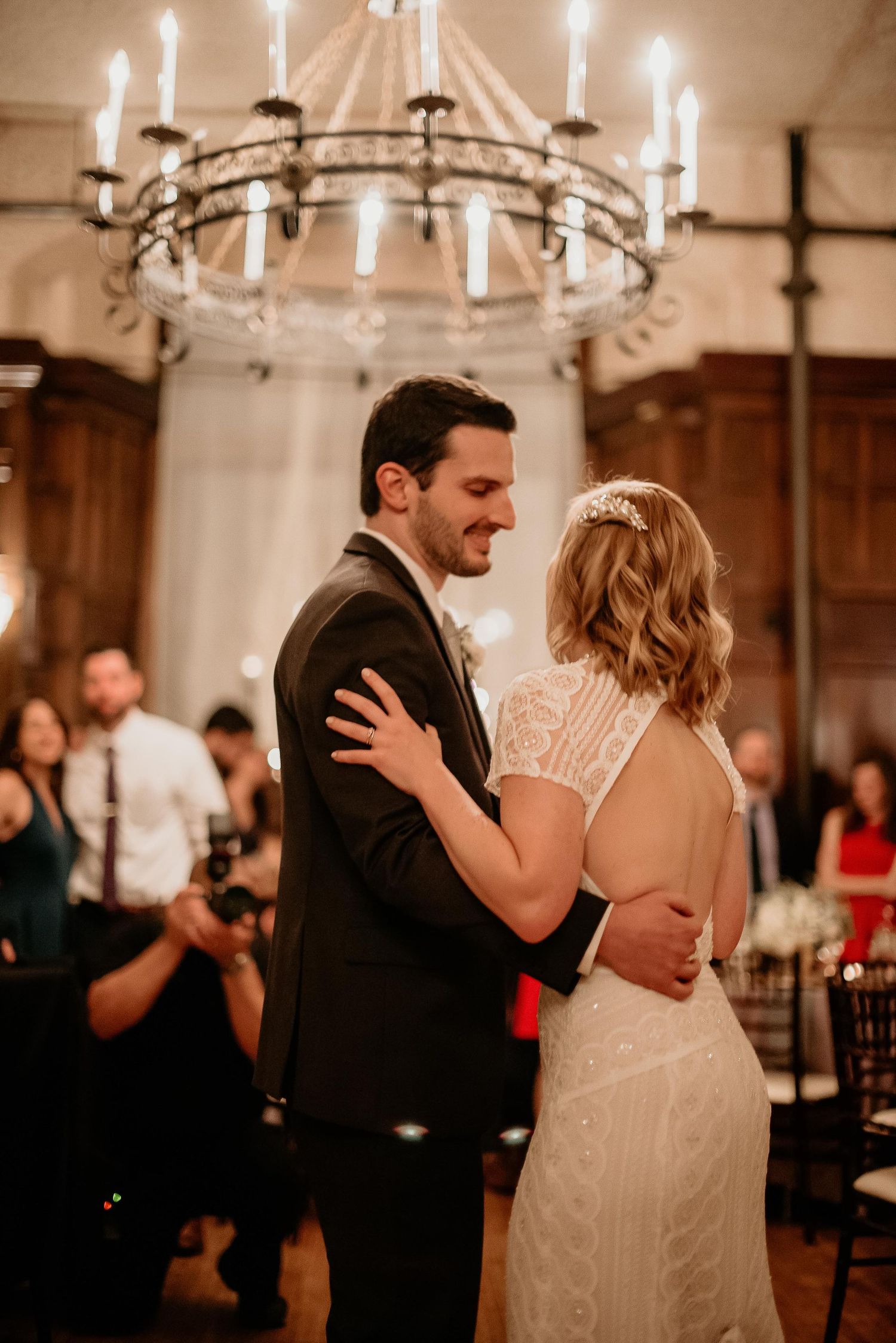 Bride and groom share their first dance under a candlelit chandelier at an elegant wedding reception.