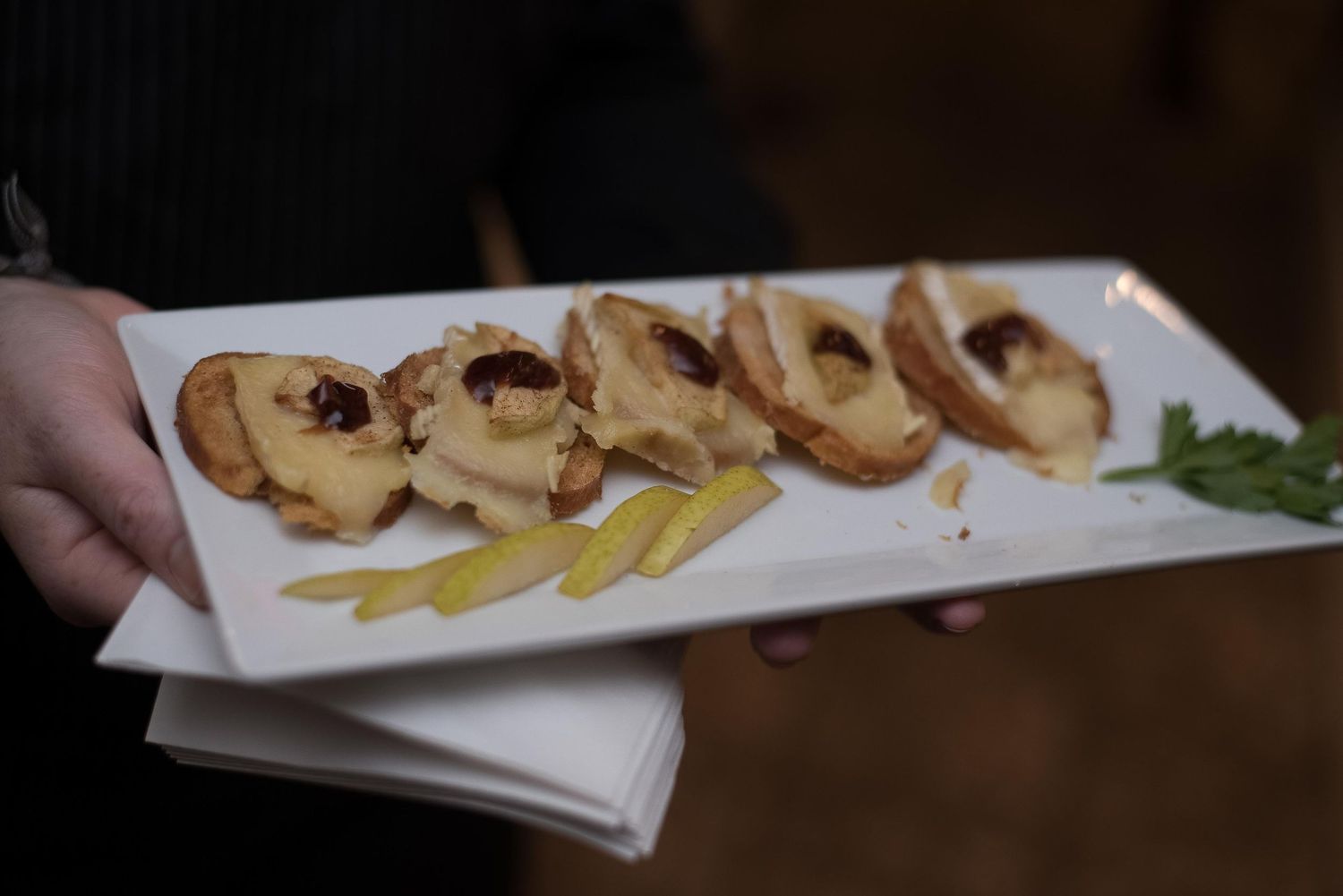 White plate of golden bruschetta topped with cheese and garnished with fresh herbs and yellow pepper strips.