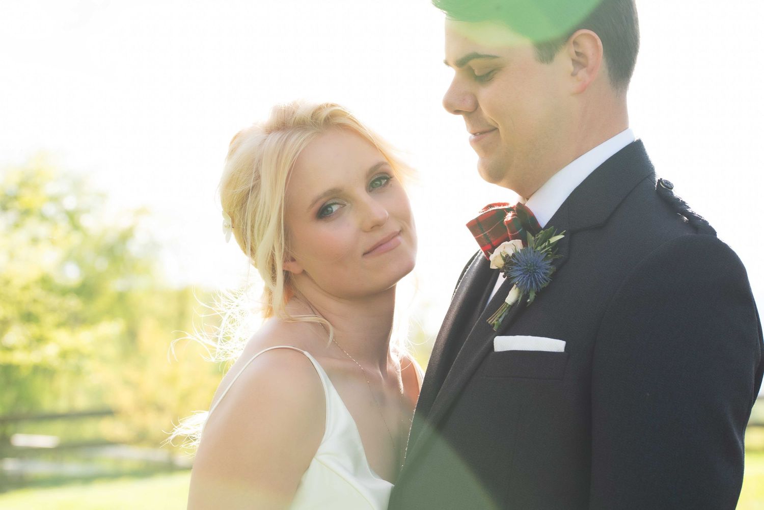 A bride and groom share a romantic moment outdoors, with soft sunlight glowing behind them on their wedding day.
