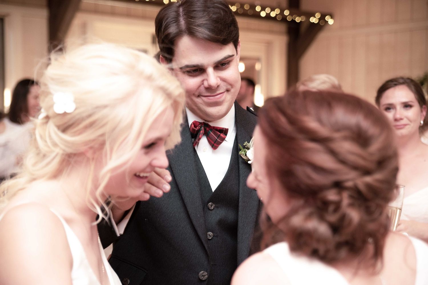 Groom in black tuxedo smiling at bride in white dress during wedding reception celebration.