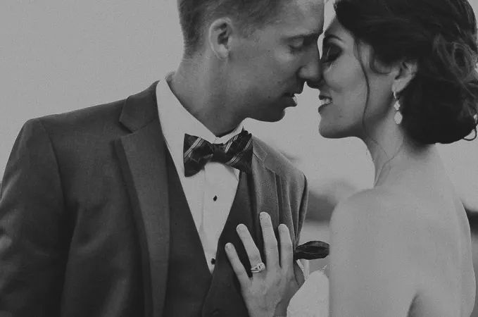 Black and white romantic portrait of bride and groom in tuxedo nearly kissing closely.
