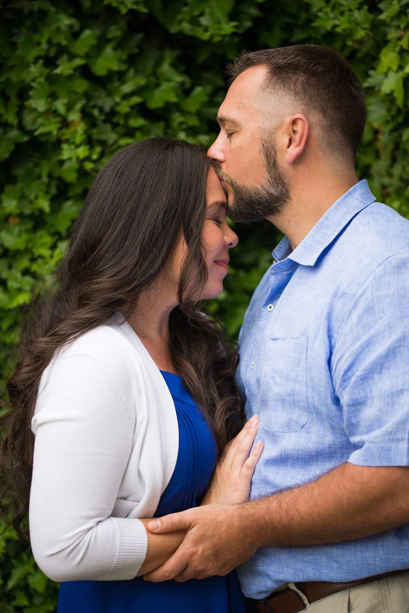 Couple sharing a tender almost-kiss moment surrounded by lush green ivy wall backdrop.